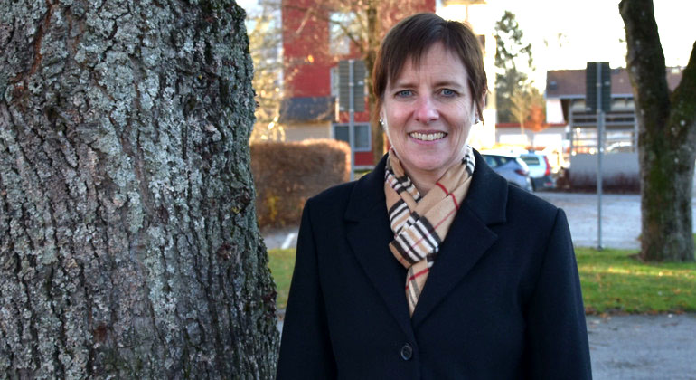 Anna Efraimsson står bredvid ett träd och ler mot kameran. Hon har en svart jacka på sig och en beige halsduk.