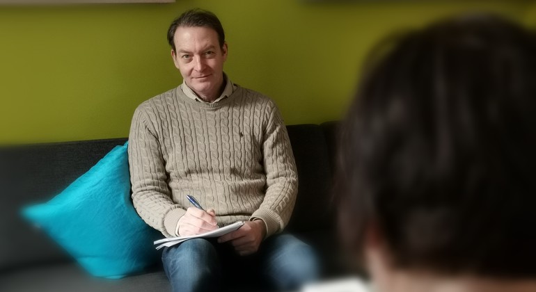 En person sitter på en soffa och antecknar.