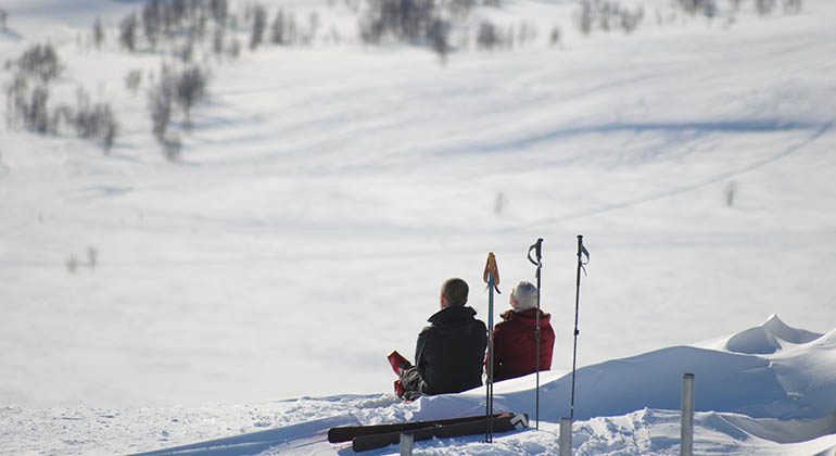 Två personer sitter i en backe i fjällen och fikar