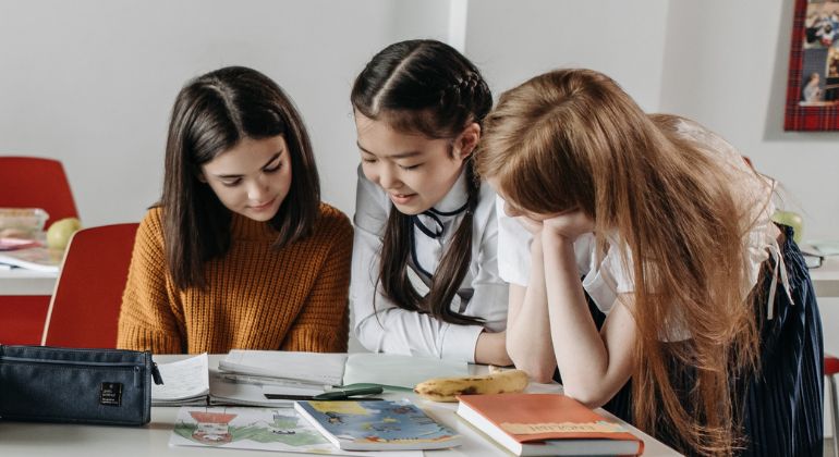 Tre glada barn kollar ner på skolbänken