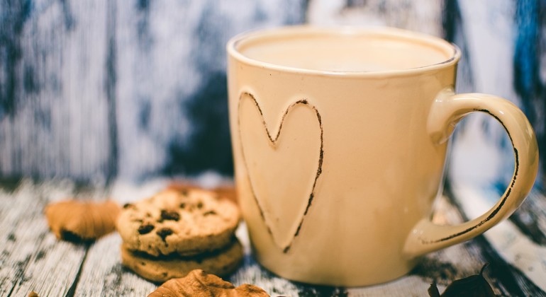 Kaffemugg med ett hjärta på. Det befinner sig även kakor bredvid och ett höstlöv.