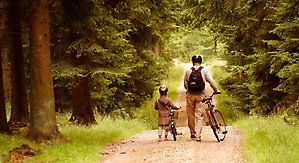 Bar och vuxen går med cyklar längst en skogsväg
